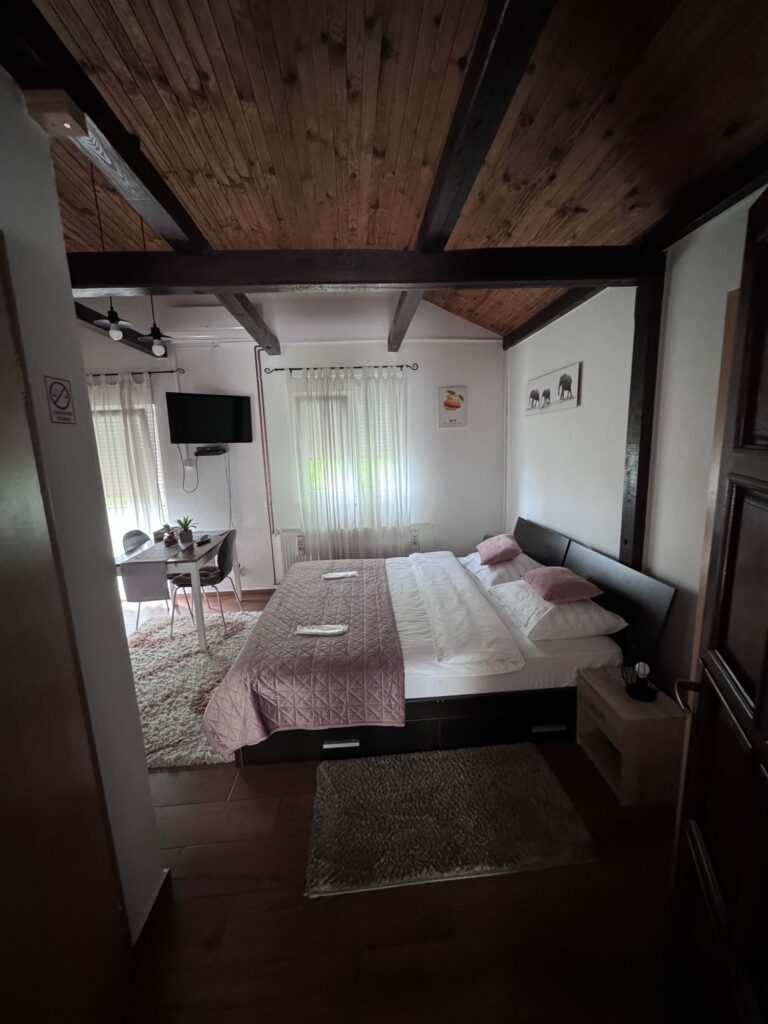 pogled na bračni krevet, kuhinjski stol s dvije stolice i televizorom na zidu u apartmanu djed