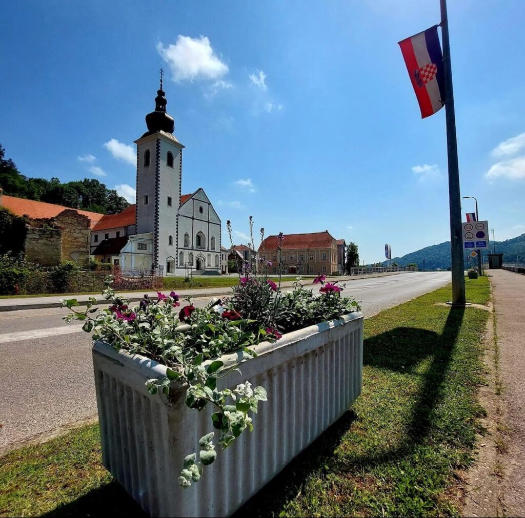žardinjera cvijeća i iza nje crkva svetog Antuna Padovanskog u Hrvatskoj Kostajnici