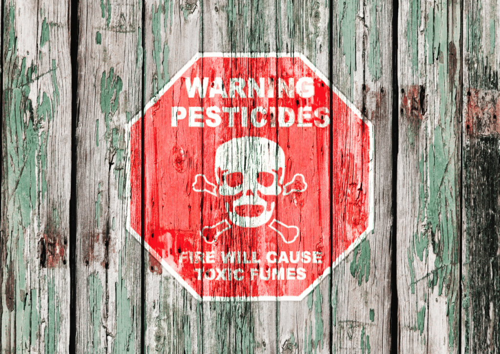 crveni znak na zelenkastoj drvenoj ograni na kojem piše upozorenje pesticidi i stavljena je mrtvačka glava